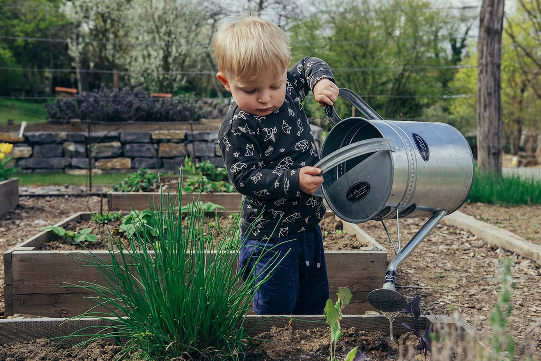 little boy watering a raised garden bed.  Raised garden beds sold at Green Living Supply