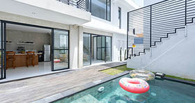 White house with large window leading to the interior and swimming pool outdoors
